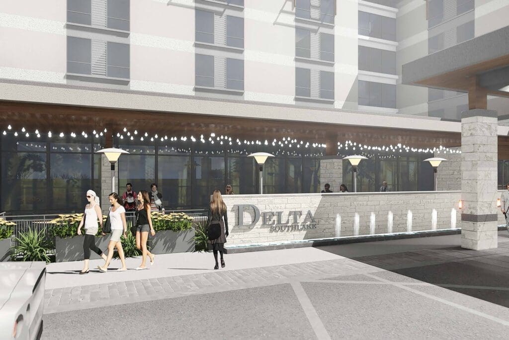 Street view of a hotel entrance with "Delta" signage. Several people walk along the sidewalk, and others are near the entrance. The building features a row of lights and modern architectural elements.