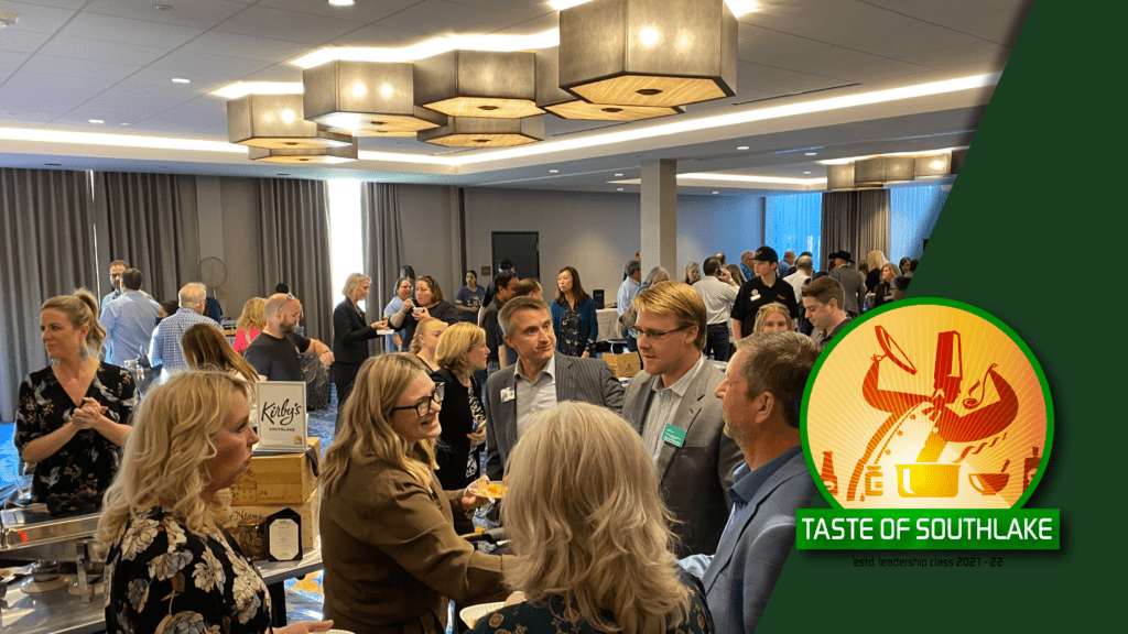 A bustling indoor event with people mingling and sampling food at various booths. There are modern ceiling lights, and a large green logo in the foreground reads "Taste of Southlake" with utensils depicted.
