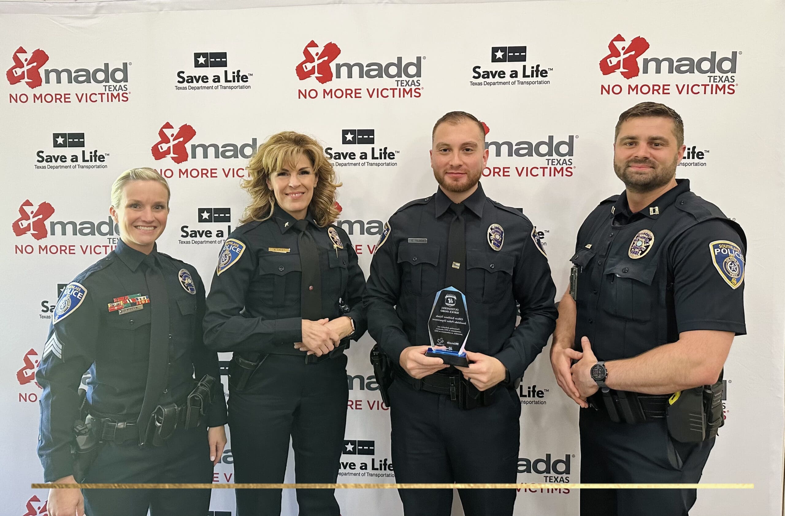 Four police officers in uniform stand in front of a backdrop with "MADD Texas" and "Save a Life" logos. The officer in the center holds an award plaque. The group is smiling and posing for the photo.