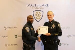 Two police officers are shaking hands, one is holding a certificate. Both are wearing uniforms with badges. The backdrop displays the Southlake Police logo and text.