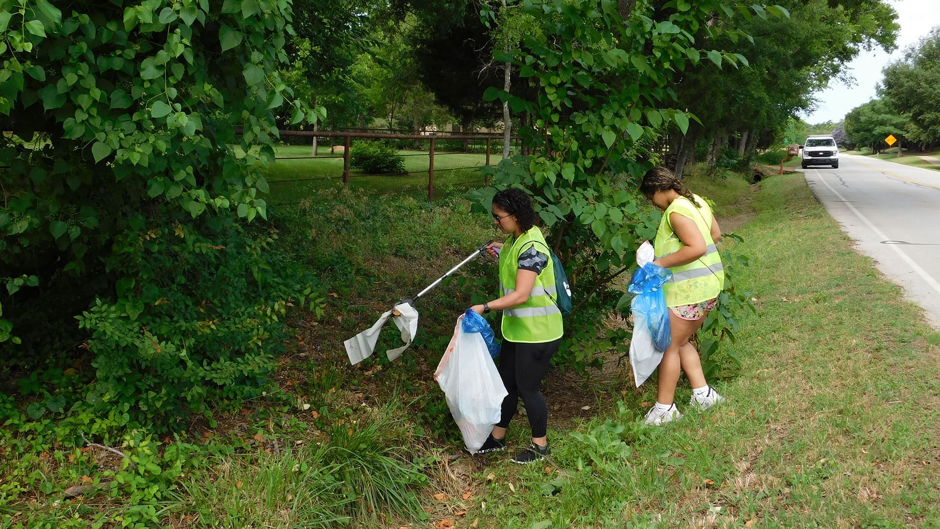 Image of two volunteers picking up trash on the side of the road