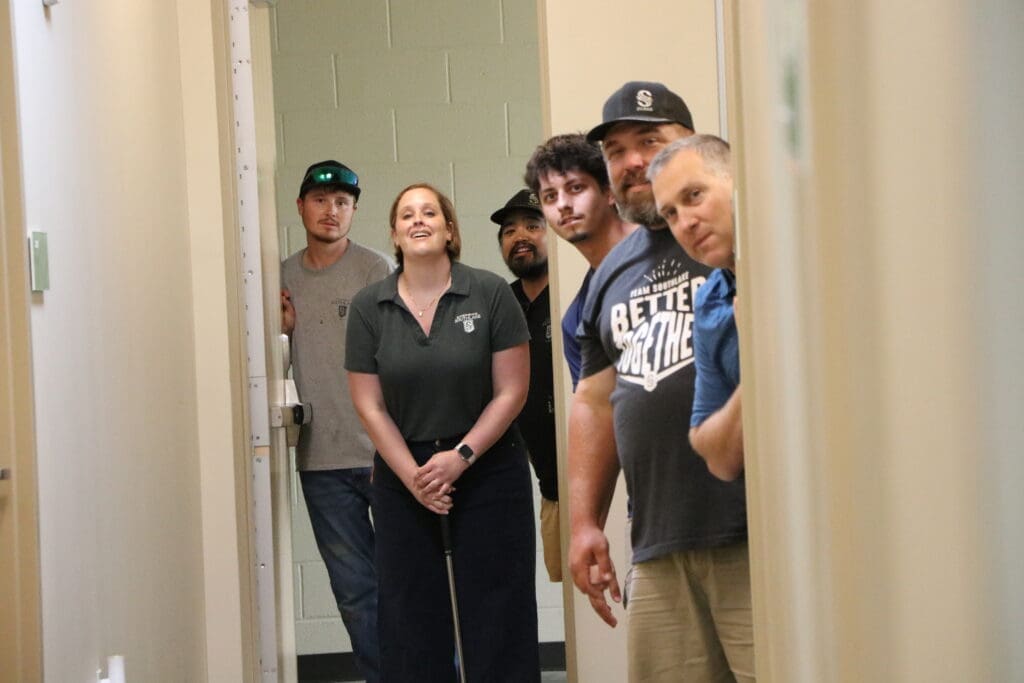 Members of a team peering into a hallway and smiling