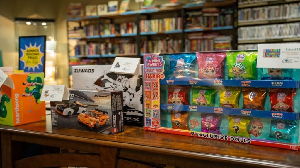 Picture of prizes for Summer Reading with books in the background. The prizes shown are Mini Sweet Haribo and a Lego McLaren set.