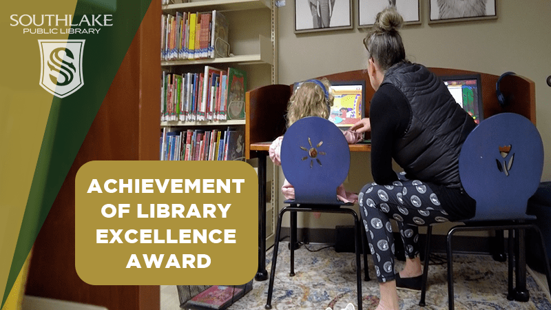 A woman and child sit at computers in a library. A sign reads "Achievement of Library Excellence Award." Bookshelves filled with books are in the background.