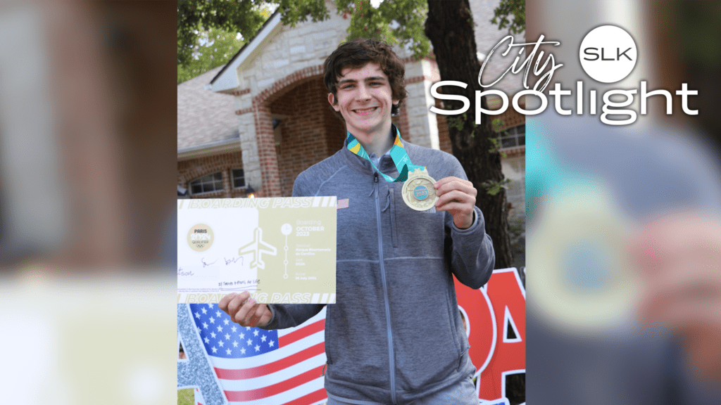 A young man in a gray jacket holds a medal and a boarding pass with a smile. A house and trees are in the background. The image features the text "City Spotlight" and "SLK" in the top right corner.