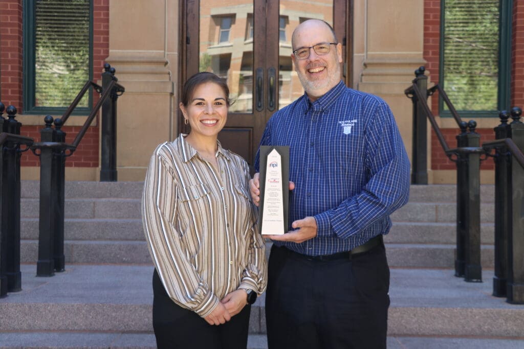 Two people smiling for a photo while holding an award