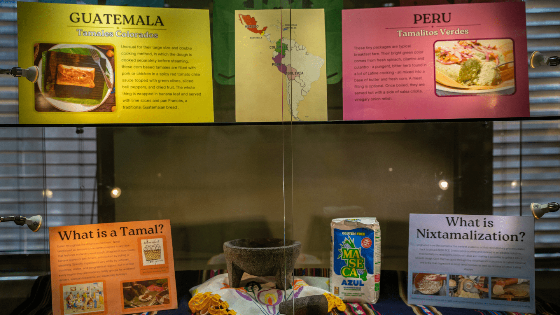 The image shows a display case with signs showcasing different foods from different countries. The counties in this particular display are Guatemala, Peru and details on what a Tamal is as well as Nixtamalization.