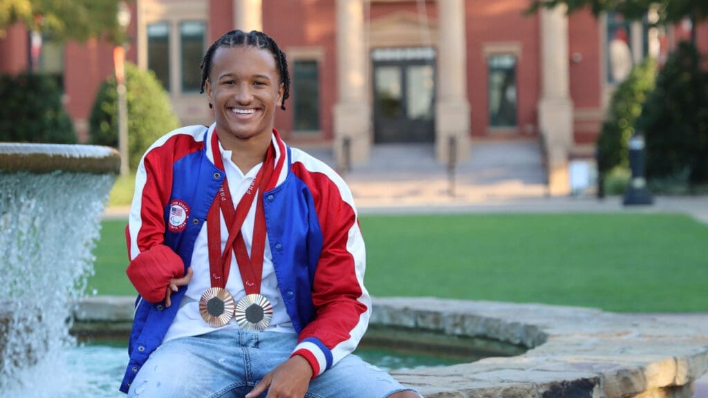 Photo of a man sitting on a bench with medals around his neck