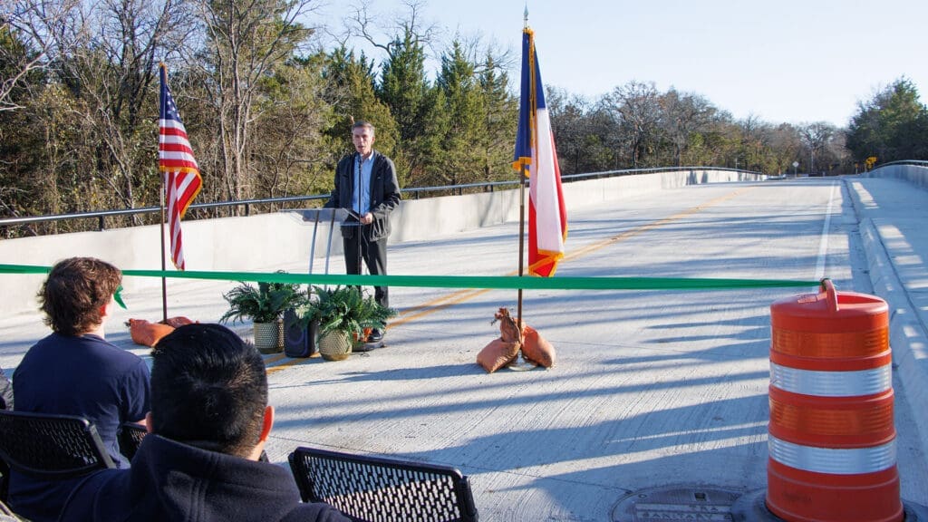 Photo of a man speaking in front of a green ribbon
