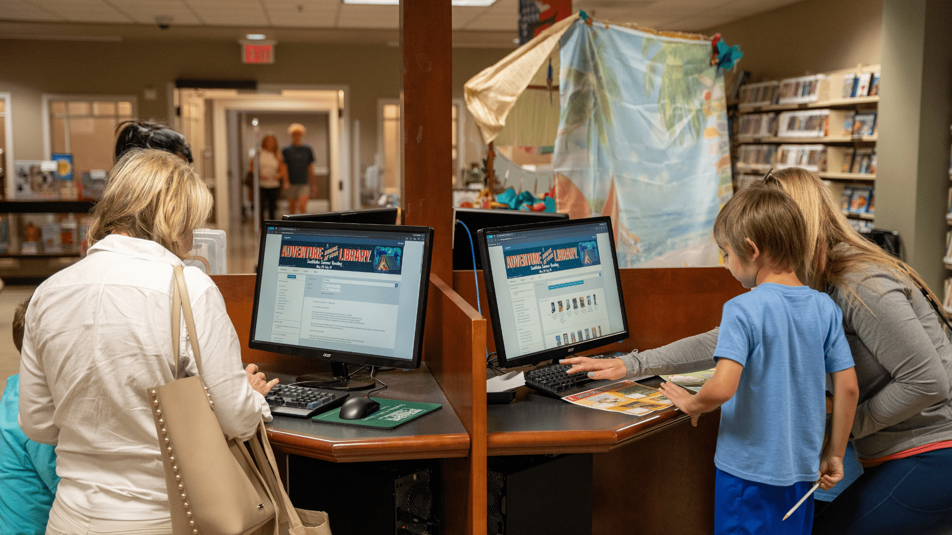 Image shows parents standing next to kids on library computers.