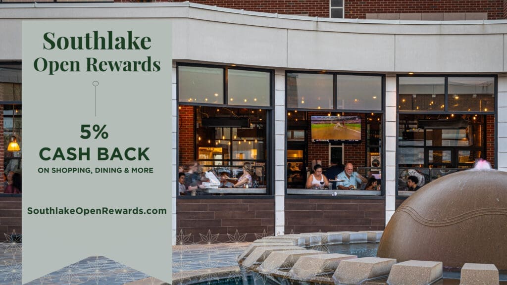 Restaurant with outdoor seating and a water fountain in the foreground. A sign promotes "Southlake Open Rewards" offering 5% cash back on shopping and dining, with a web address: SouthlakeOpenRewards.com. Lights are visible inside the restaurant.