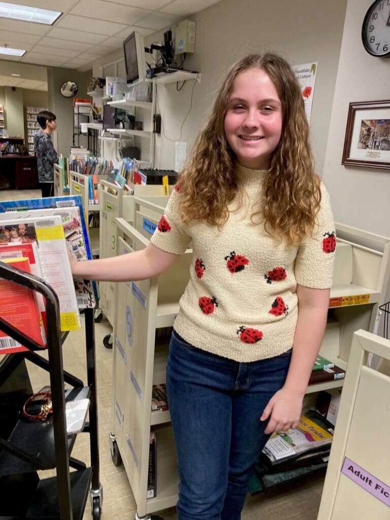A woman beside a book shelf.