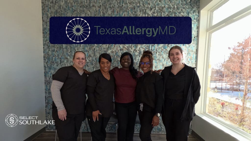 Five people in black clothing stand smiling in front of a mosaic wall with a "TexasAllergyMD" sign. The setting has a modern look with a large window on the right. The "Select Southlake" logo is visible at the bottom left.