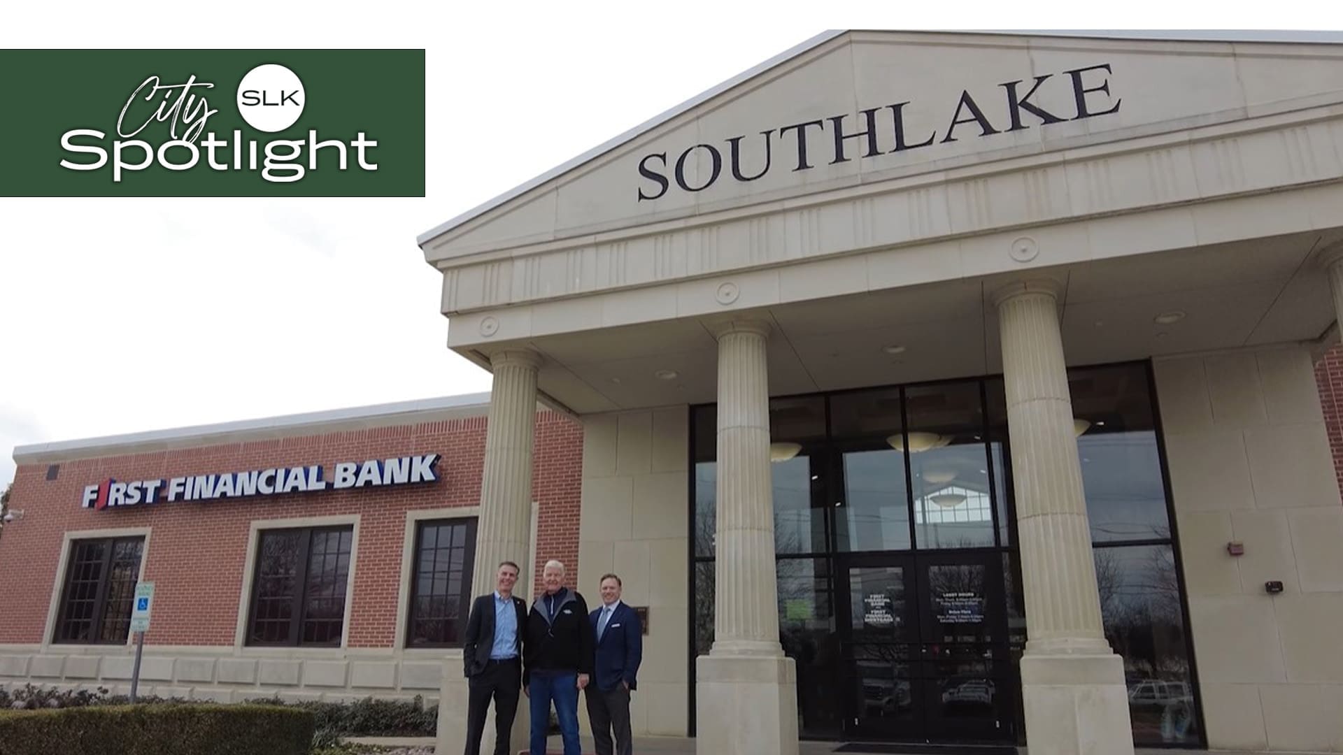 Mayor Shawn McCaskill, Shelby Bruhn, and Wayne Lee stand in front of a building with large pillars labeled "SOUTHLAKE." To the left, a brick building is marked "FIRST FINANCIAL BANK." The upper left corner features the text "City SLK Spotlight" on a green background.