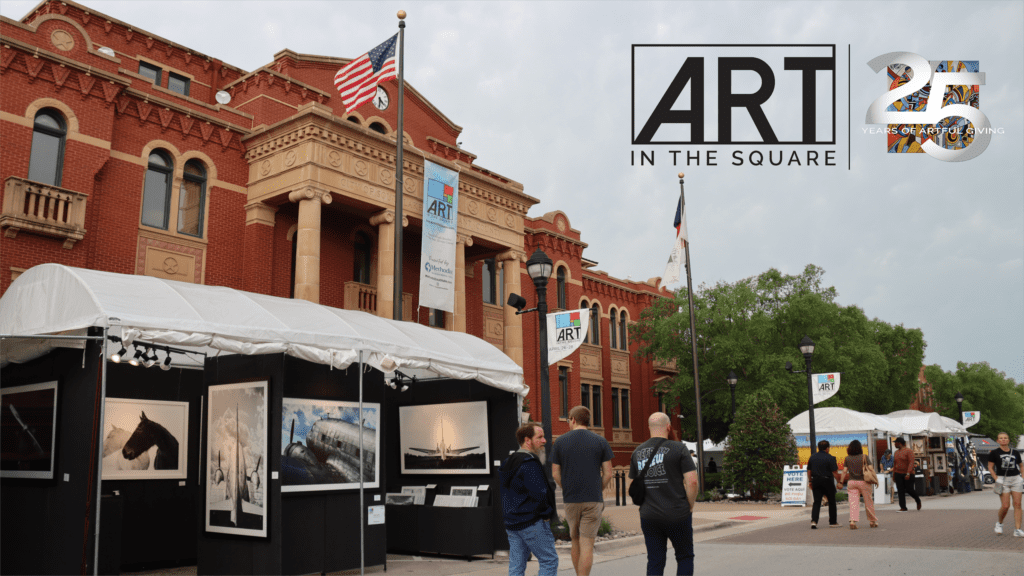 People walk past art displays in white tents outside a historic red-brick building with columns. Banners read "ART IN THE SQUARE" and "25 Years of Creativity." An American flag waves atop the building.