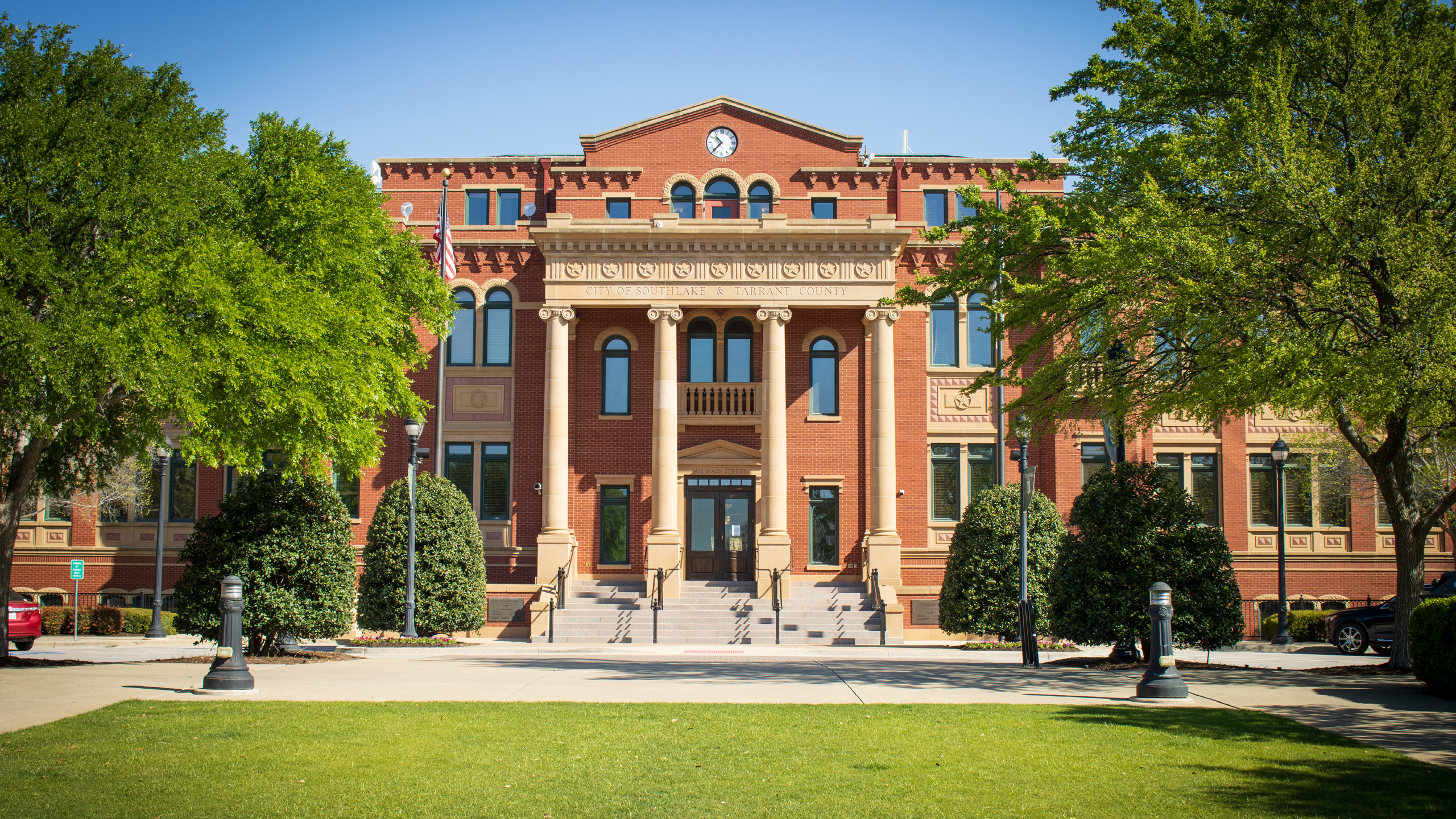 A government building sits behind a grassy area with trees.