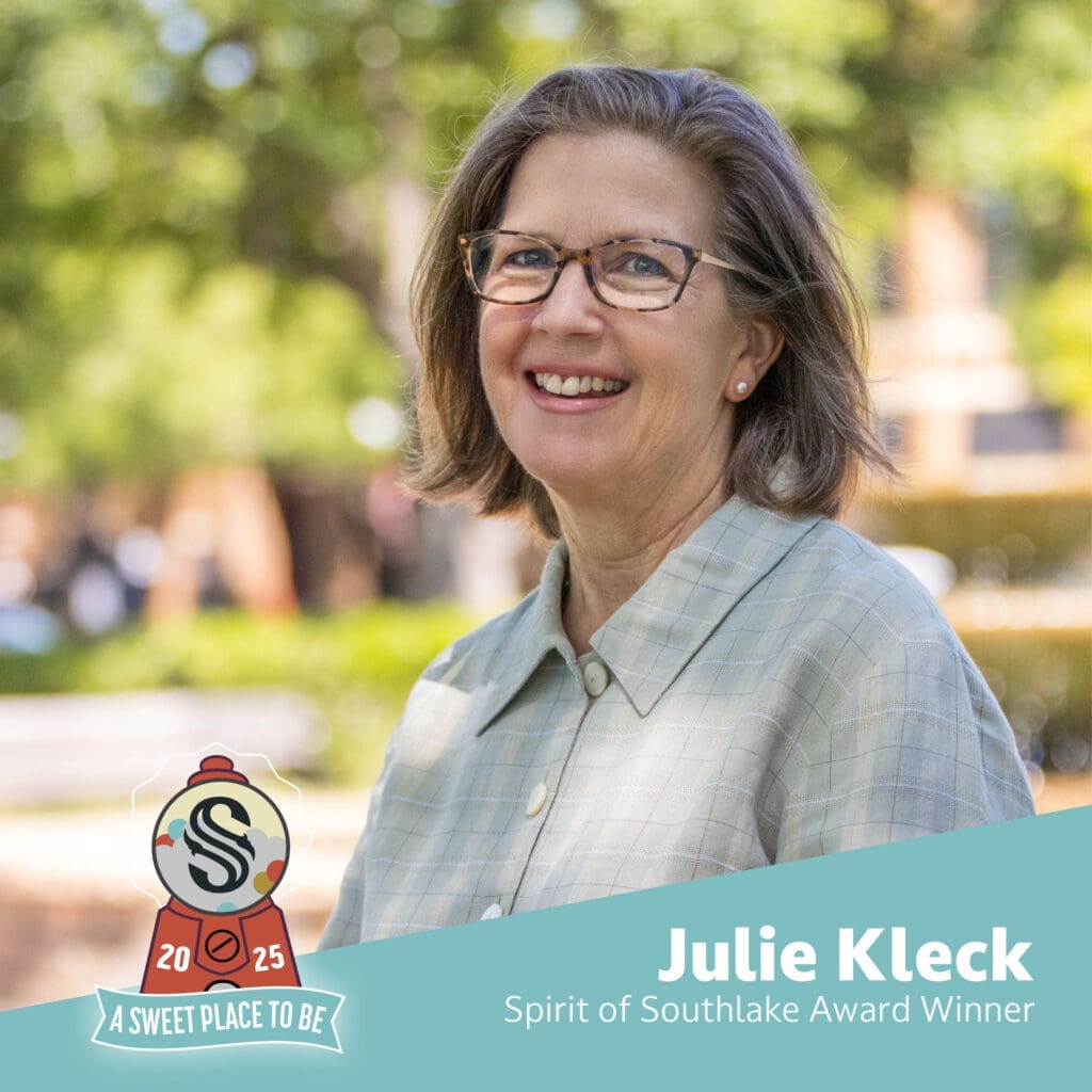 A smiling woman with shoulder-length brown hair and glasses stands outdoors. She wears a light green button-up shirt. Text reads: "Julie Kleck, Spirit of Southlake Award Winner" and "A Sweet Place to Be.