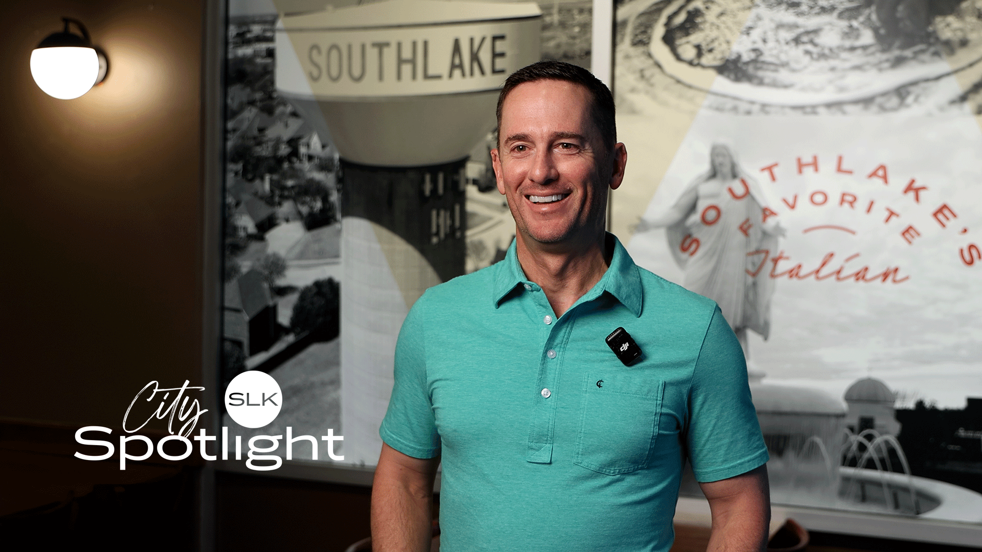 A smiling man in a teal polo stands indoors with a microphone clipped to his shirt. Behind him are images and text referencing Southlake, including "Southlake's Favorite Italian." City Spotlight SLK logo is in the lower left.