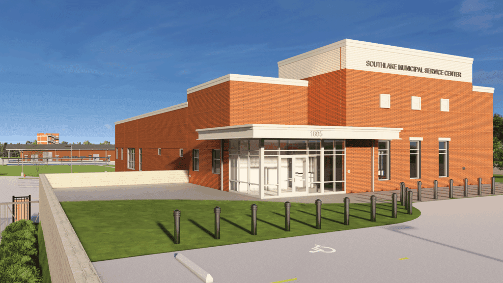 A modern red-brick building labeled "South Ave Municipal Service Center" sits under a blue sky, featuring large windows, a small covered entrance, and a paved driveway. Another building and green lawn are visible in the background.