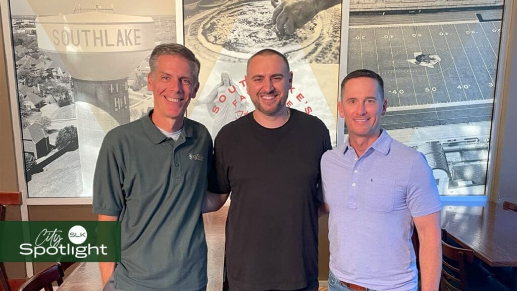 Three men stand smiling indoors in front of a wall with Southlake-themed images, including a water tower and football field. The City Spotlight SLK logo is in the bottom left corner.