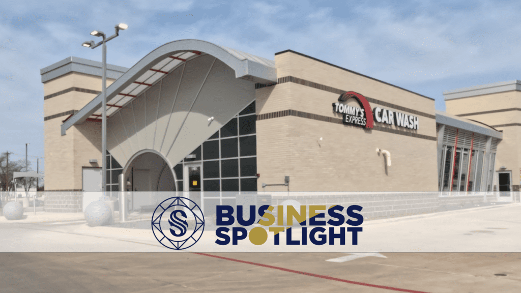 A modern Tommy’s Express Car Wash building with tan brick walls and a curved metal roof. The “Business Spotlight” logo and text are overlaid at the bottom of the image.