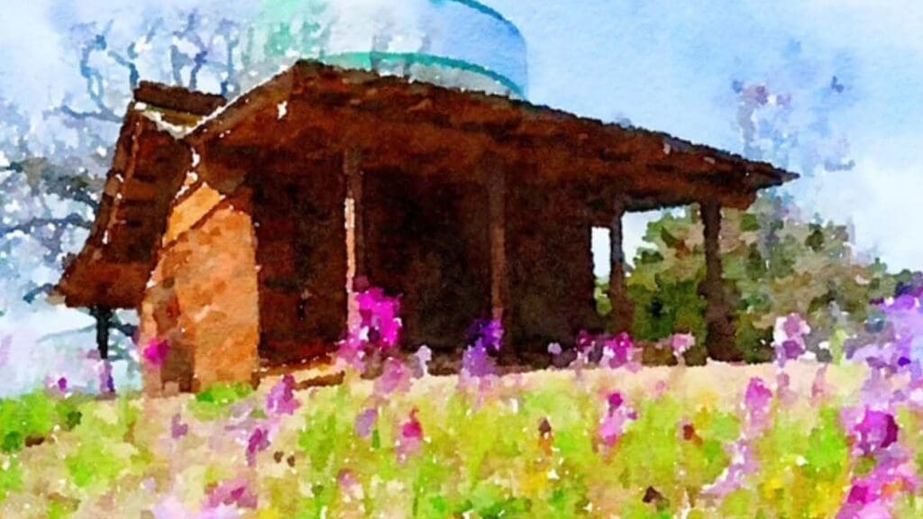 A watercolor-style image of a small wooden cabin with a slanted roof, surrounded by green grass and blooming pink and purple flowers, set against a blue sky with scattered clouds.