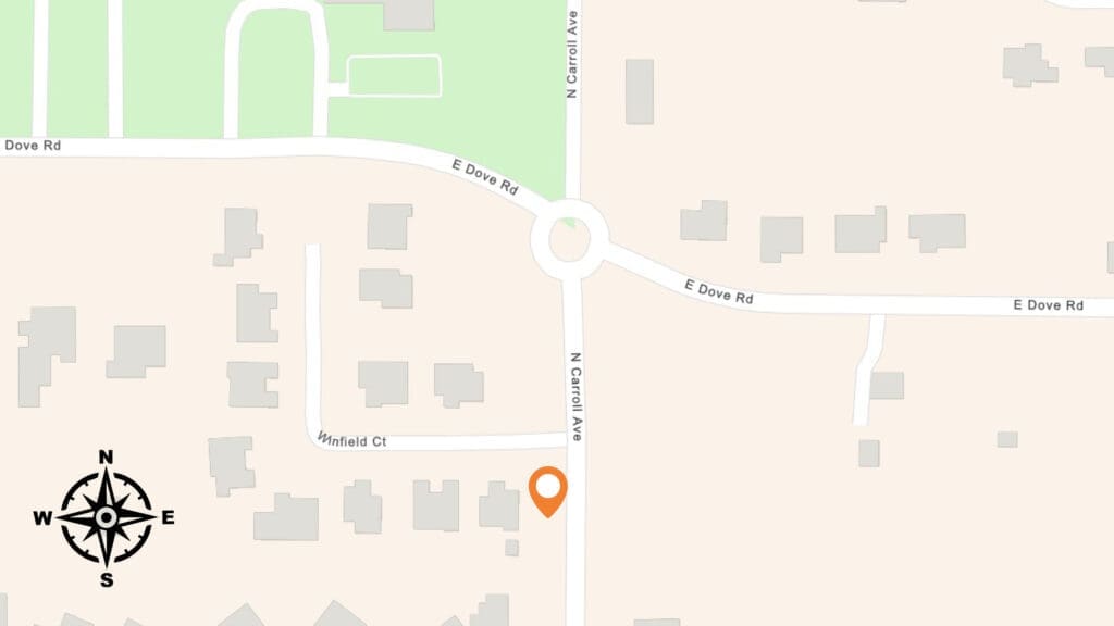 Map showing the intersection of E Dove Rd and N Carroll Ave with a roundabout. An orange location pin is placed on Windfield Ct, southwest of the intersection. A compass rose is in the lower left corner.